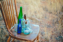 old glass bottles on a wood chair outdoors 
