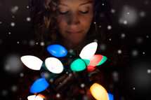 woman holding a strand of glowing Christmas lights 