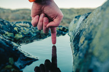 a finger touching a puddle of pooled water 