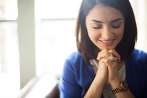 A young woman with hands clasped in prayer.