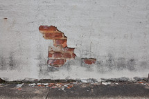 Red brick showing through broken plaster on a wall.