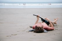 man lying on a beach playing a ukulele 