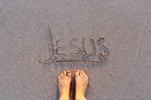 Jesus written in the sands of a beach and bare feet 