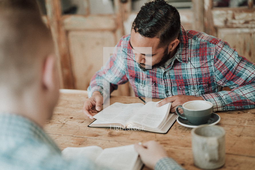two men reading Bibles and discussing scripture sitting at a table 