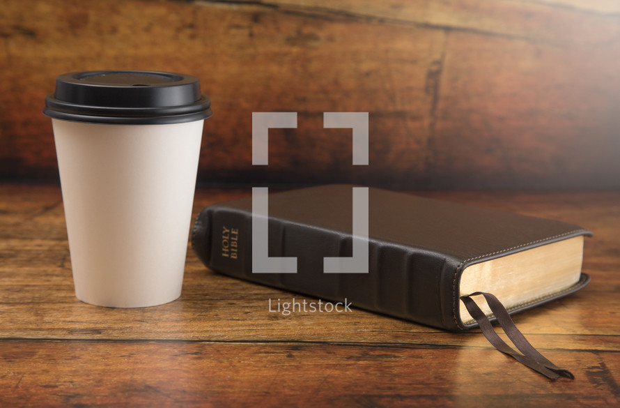 Bible and Disposable White Coffee Cup with Black Lid on a Wood Background