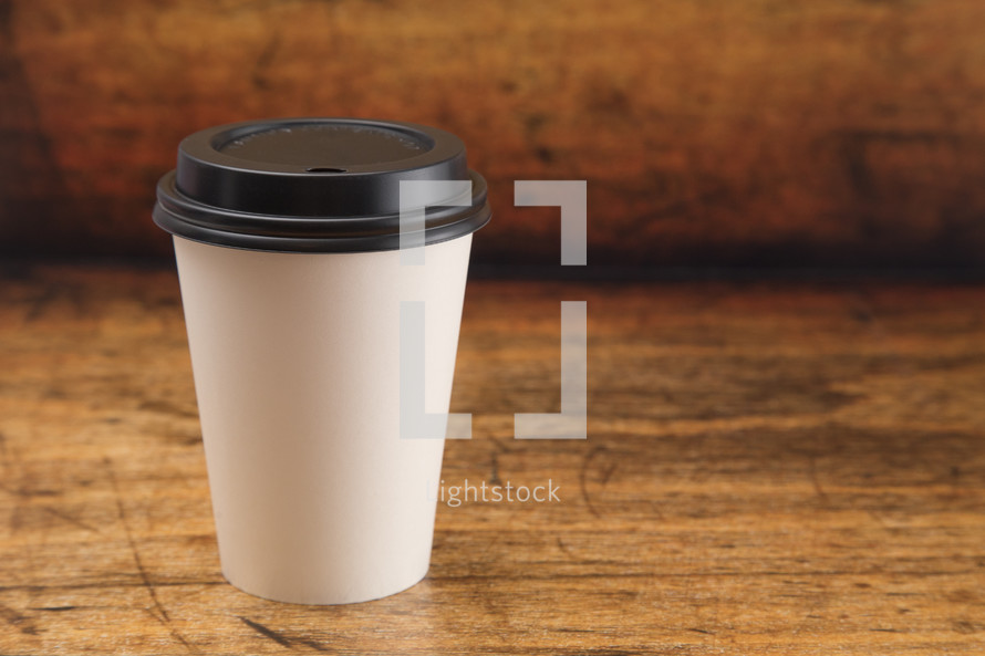Disposable White Coffee Cup with Black Lid on a wood Background