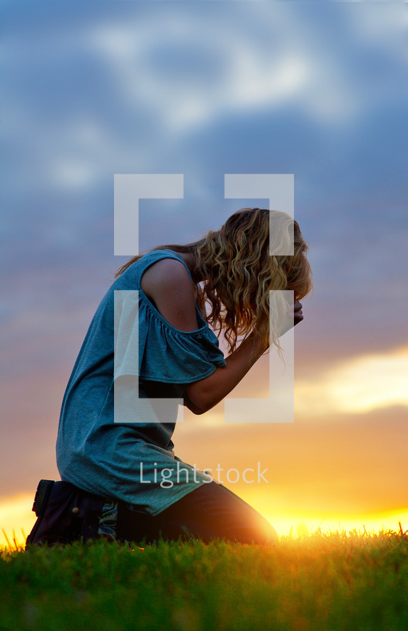 a woman kneeling in prayer at sunset 