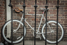 a parked bike leaning against a brick wall behind a wrought iron fence 