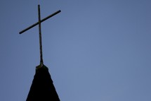 Silhouette of a church steeple with a cross in the moonlight.