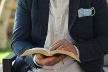 a man holding a Bible with a face mask in his pocket 