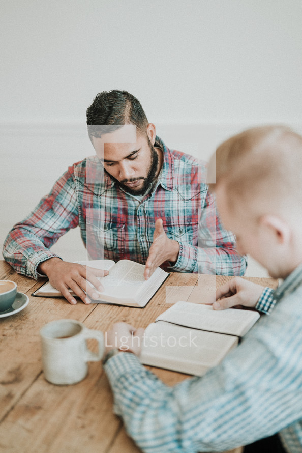 two men reading Bibles and discussing scripture sitting at a table 