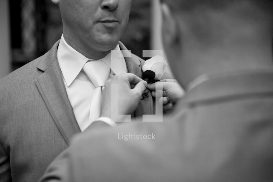 A groomsman pins a boutonniere to a groom's lapel.