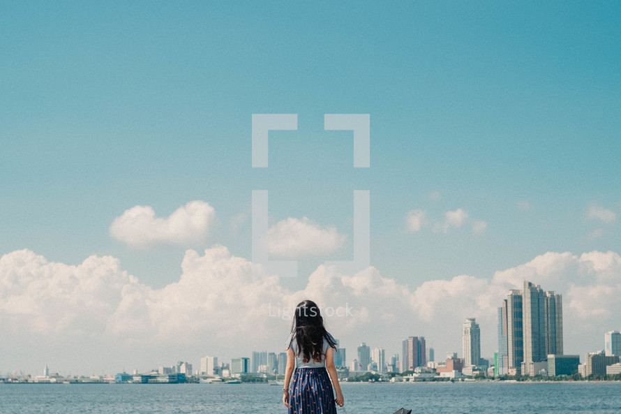 a girl looking across a bay at a city 