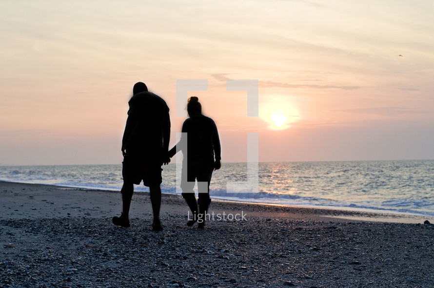 silhouette of a couple walking holding hands on the beach
