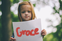 Child holding a handwritten sign saying, "Grace."