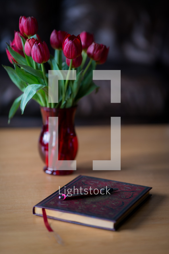 A vase of red tulips on a table next to a journal and pen.
