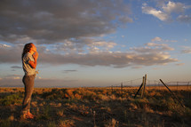 teen girl praying in a field at sunset 