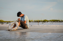 man in prayer on a beach and a life ring