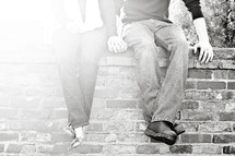 couple holding hands sitting on a brick wall