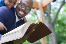 A smiling father and young son reading the Bible.