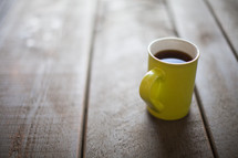 A yellow cup full of coffee on a wooden table.