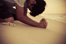 man kneeling in prayer on a beach