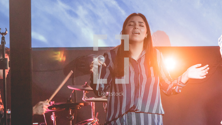 a woman singing on stage during a worship service 