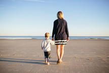 mother and son walking holding hands on a beach 