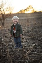 A toddler boy standing in a plowed field. 