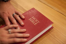 Hands of a husband and wife on a red Bible.