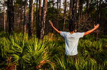 man standing in a field of palms with his hands raised 
