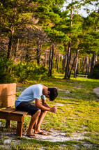 man sitting in prayer on a bench outdoors