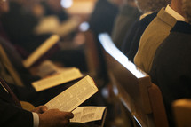 parishioners sitting in church pews with open hymnals and worship books 
