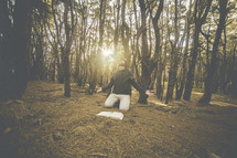 a man kneeling in prayer in a forest near an open Bible 