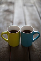 Yellow and blue cups of coffee on a wooden table.