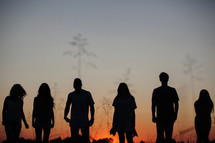 silhouettes of people standing outdoors at sunset 