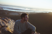 Man sitting on a rocky hill at the beach.