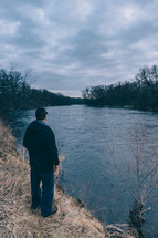 a man standing on a riverbank under an overcast sky