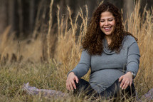 a pregnant woman sitting in a field of tall grass 