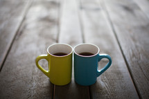 Yellow and blue cups filled with coffee and on a wooden table.