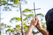 man holding a cross made from sticks in the air 
