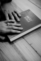 Husband and wife's hands on a Bible.