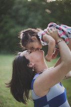 Woman holding and kissing her daughter outside.
