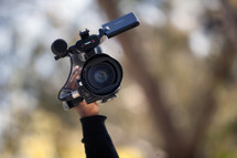 A video camera being held high.