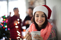 A smiling woman wearing a santa hat and holding a cup of coffee