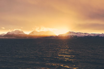 snow covered mountain peaks at sunset and ocean water