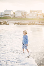blonde boy child standing in the sand on a beach 