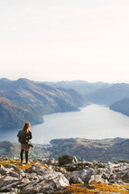 a young woman standing on a mountaintop looking down at a lake 