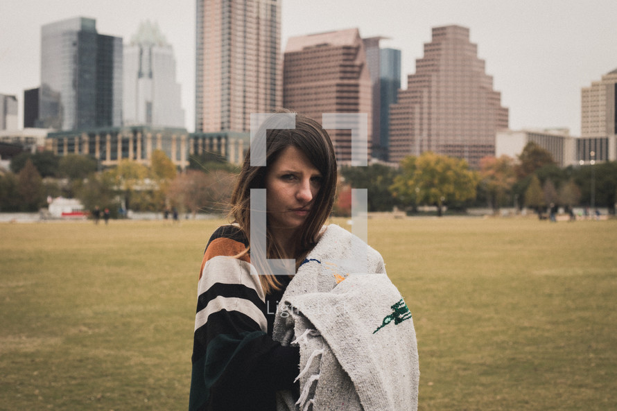 a woman standing in a city park holding a blanket 