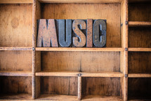 Wooden letters spelling "music" on a wooden bookshelf.